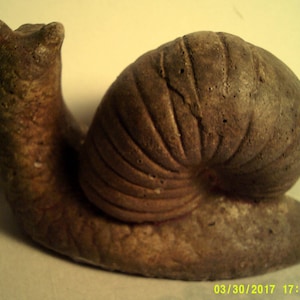 May include: A brown ceramic snail sculpture with a detailed shell and a textured body.
