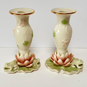 Peut inclure: Une paire de bougeoirs en céramique blanche avec un bord doré. Chaque bougeoir présente une fleur de lotus rose avec des feuilles vertes et une grenouille sur une base de feuille.