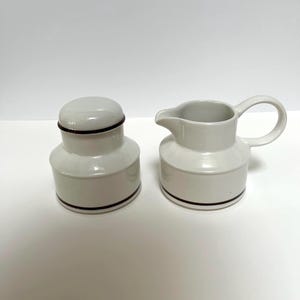 Peut inclure: Ensemble de crémier et sucrier en céramique blanche avec une bande brune autour du haut de chaque pièce.