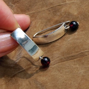 May include: A pair of silver earrings with a curved bar design and a dangling red gemstone bead.