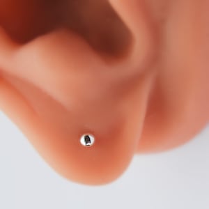 May include: A close-up of a small, silver ball stud earring in a person's ear.