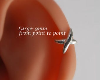 May include: A silver-colored ear cuff with a cross-like design. The text "Large - 9mm from point to point" is visible. The cuff is shown on an ear.