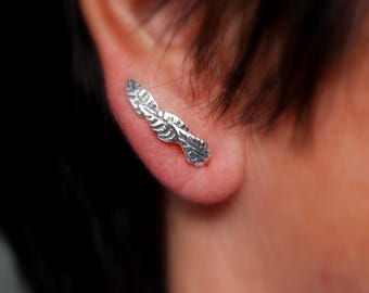 May include: Silver ear cuff with a leaf design. The cuff is curved and has a textured surface.