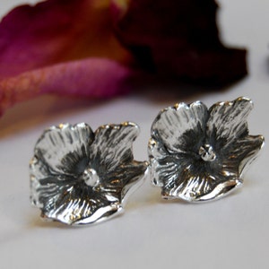 May include: A pair of silver flower stud earrings. The earrings are made of sterling silver and feature a detailed floral design.