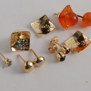 May include: A set of six gold earrings with various gemstones. The earrings feature a variety of styles, including square, round, and teardrop shapes. The gemstones are blue, red, and orange.