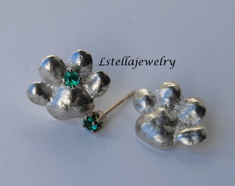 May include: A pair of silver paw print earrings with a green gemstone in the center of each paw print. The earrings are on a white background.