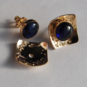 May include: A pair of gold earrings with blue gemstones. The earrings have a textured, hammered finish.