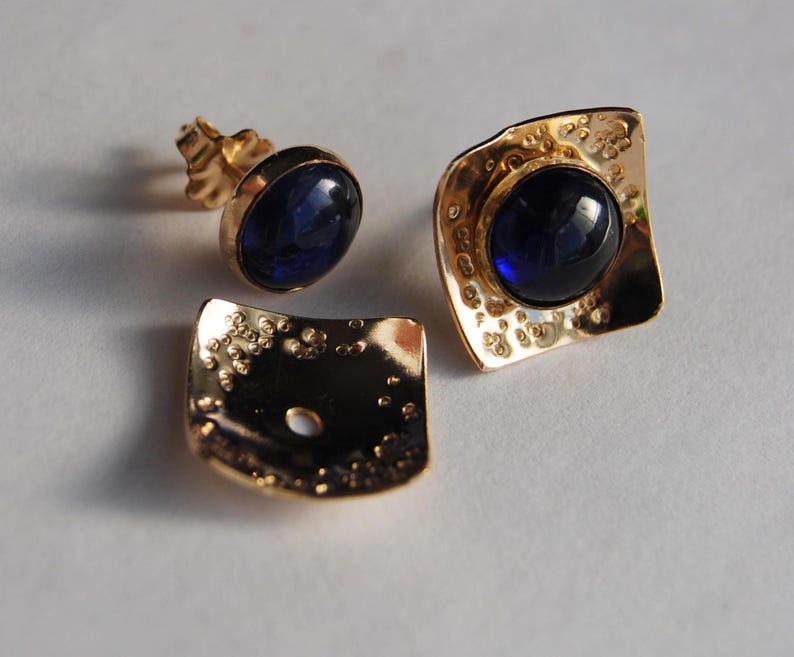 May include: A pair of gold earrings with blue gemstones. The earrings have a textured, hammered finish.