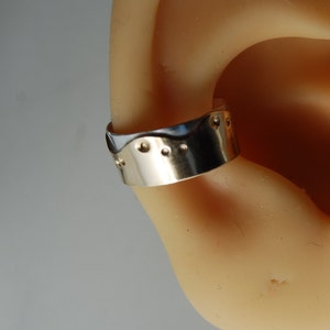 May include: A silver ear cuff with a wavy design and small dots along the edge.