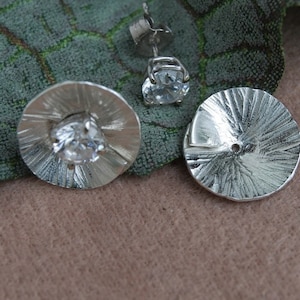 Peut inclure: Une paire de boucles d'oreilles en argent avec un design circulaire texturé. Une boucle d'oreille présente une pierre précieuse ronde transparente au centre.