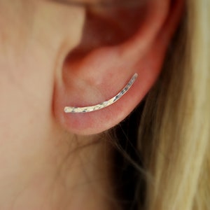 May include: A silver ear cuff with a hammered finish. The cuff is curved and has a simple design.