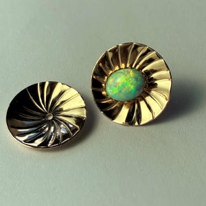 May include: A pair of gold-colored stud earrings. One earring features a vibrant green opal gemstone set in a sunburst design. The other earring is a matching gold-colored disc with a spiral pattern.