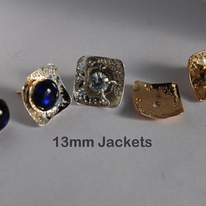 May include: Four earring jackets, two with a silver finish and two with a gold finish. The silver jackets have a clear stone in the center, and the gold jackets have a clear stone in the center. The text "13mm Jackets" is printed below the earrings.