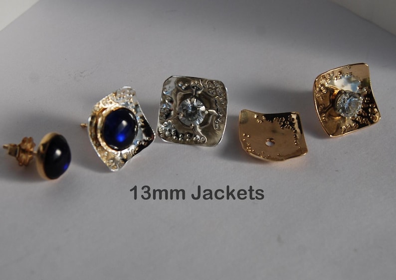 May include: Four earring jackets, two with a silver finish and two with a gold finish. The silver jackets have a clear stone in the center, and the gold jackets have a clear stone in the center. The text "13mm Jackets" is printed below the earrings.