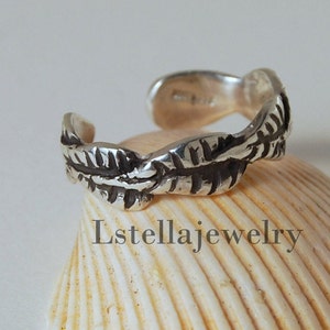 May include: Silver toe ring with a leaf design. The ring is open and adjustable.