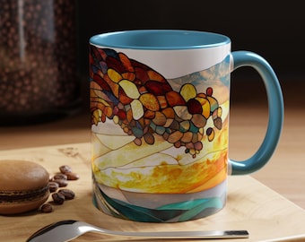 May include: A blue and white ceramic mug with a stained glass design of a mountain range. The mug has a blue rim and handle.