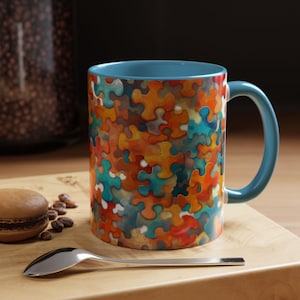 May include: A blue ceramic coffee mug with a colorful jigsaw puzzle pattern. The mug has a rounded handle and a white interior.