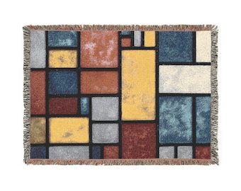 May include: A rectangular throw blanket with a geometric design. The pattern features various rectangular shapes in shades of yellow, blue, gray, and red, outlined in black. The blanket has a fringed edge.