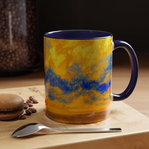May include: A blue and yellow ceramic mug with a swirling abstract design. The mug has a dark blue rim and handle.