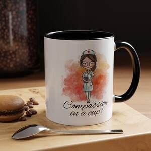 May include: White ceramic mug with a black interior and handle. The mug features a cartoon illustration of a nurse with the text "Compassion in a cup!" against a watercolor background of red and orange.