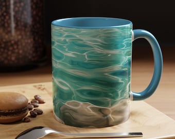 Könnte beinhalten: Eine Keramik-Kaffeetasse mit blauem Griff und Innenraum. Die Außenseite zeigt ein türkisfarbenes Wassermuster mit weißen Highlights. Die Tasse steht auf einem Holzbrett mit einem silbernen Löffel, einem Macaron und Kaffeebohnen.