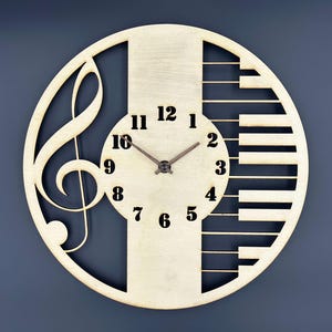 May include: A circular wooden clock with a musical design. The clock face incorporates a treble clef, piano keys, and black numerals. The clock hands are brown. The clock is crafted from light-coloured wood and has a contemporary aesthetic.