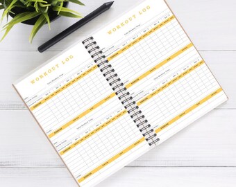 May include: A spiral-bound workout log notebook with a black pen and a small potted plant. The notebook has a white interior with yellow accents and the words "WORKOUT LOG" printed at the top. The pages are lined for recording exercises.