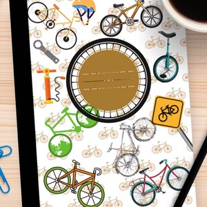 Può includere: Quaderno a tema bicicletta. La copertina presenta varie illustrazioni di biciclette in giallo, verde, arancione e rosso, insieme a un cartello stradale giallo per biciclette. Un grande cerchio marrone con linee per scrivere è al centro. Il quaderno ha un dorso nero.