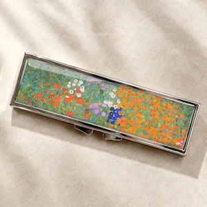 May include: A rectangular metal case with a hinged lid featuring a vibrant, colourful floral print. The design displays a dense field of small red, orange, white, purple, and blue flowers set against a green background, encased in a polished silver frame.