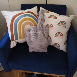 May include: A blue armchair with three pillows. Two pillows have a rainbow design, one is white with multiple rainbow patterns, and the third pillow is a crocheted middle finger.