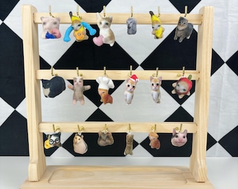 May include: A wooden display stand with three shelves holds a collection of 18 cat-themed keychains. The keychains feature various cat breeds and outfits, including a chef hat, a banana costume, and a Santa hat.
