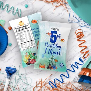 May include: Two blue and white party favor bags with an under the sea theme. One bag has a nutrition facts label and the other bag says "Happy 5th Birthday Ethan!"