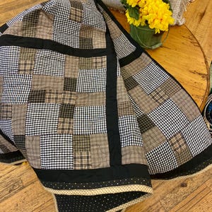 May include: A black and white checkered quilt with brown plaid squares. The quilt has a black border with a gold and black trim.