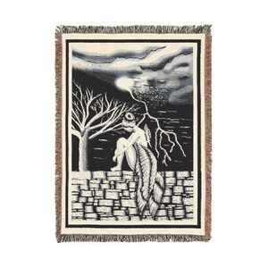 May include: Woven throw blanket featuring a black and white illustration of a person seated on a stone wall, with a tree and lightning. The blanket has a fringed border.