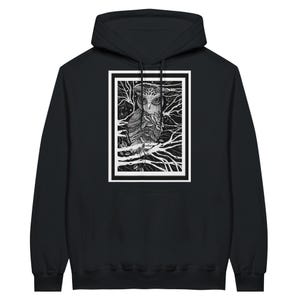 Puede incluir: Sudadera con capucha negra con una ilustración de búho en blanco y negro dentro de un rectángulo enmarcado en blanco. El búho está posado en una rama, rodeado de ramas y hojas detalladas. El diseño está centrado en la parte delantera de la sudadera.