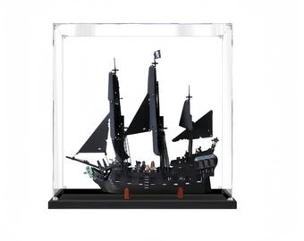 May include: A black model ship with tall masts and black sails, displayed inside a clear acrylic case. The ship has intricate details and a pirate flag. The base is black, and the case is square.