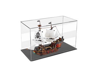 May include: A clear acrylic display case with a black base, showcasing a detailed LEGO pirate ship model. The ship features white sails, a black skull and crossbones flag, and a red and brown hull.