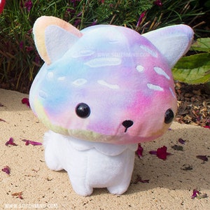 May include: A mushroom cat plush toy with a tie-dye cap in pastel shades. The cat has black button eyes and a small black nose. The white body has a scalloped collar. A cute, soft toy.