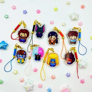 May include: A collection of colorful acrylic charms featuring cartoon characters. Each charm has a gold-colored clasp and a matching lanyard. The characters have various hair colors and outfits, with a variety of facial expressions.