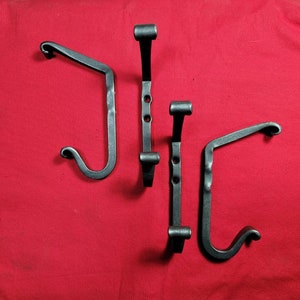 May include: Three black metal hooks with a decorative swirl design. The hooks are arranged in a row on a red background.