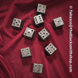May include: Nine silver metal dice with black dots on a red velvet surface.  The dice are scattered randomly on the surface.