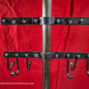 May include: A metal stand with two horizontal bars and hooks. The stand is made of black metal and has a silver pole in the center. The stand is mounted on a red background.