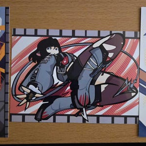 May include: Three anime-style art prints. The first features a figure in black and orange with a dynamic background. The second shows a character in gray and maroon. The third depicts a girl in an orange shirt and blue hat, with the word "STELL" visible.