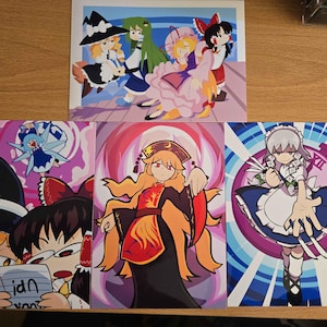 May include: Set of four colorful anime-style art prints. The prints feature various female characters in detailed costumes, with vibrant backgrounds of pink, purple, and blue. One print shows a group of characters, while the others are individual portraits.