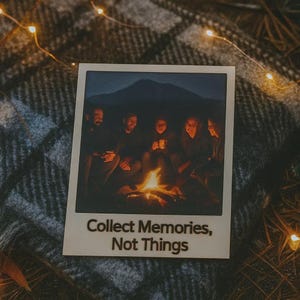 Può includere: Una fotografia in stile Polaroid mostra un gruppo di persone riunite attorno a un falò di notte, con una sagoma di montagna sullo sfondo. La foto ha il testo "Collect Memories, Not Things". La foto è su una coperta a quadri grigia e nera.
