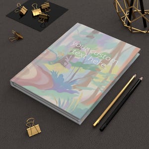 May include: A hardcover journal with a colorful abstract floral design and the text "your custom text here". Gold and black pencils and gold binder clips are next to the journal on a dark gray surface.