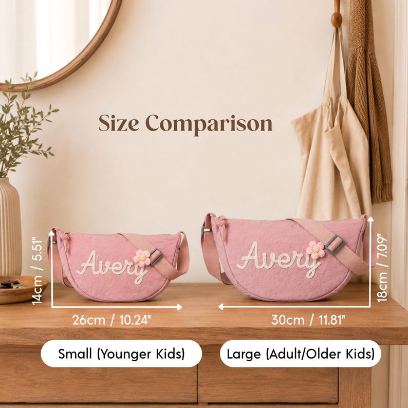 May include: Two pink crescent-shaped crossbody bags with the name Avery embroidered in white and a small flower patch. The small bag measures 10.24 inches by 5.51 inches, and the large bag measures 11.81 inches by 7.09 inches. Text reads Size Comparison.