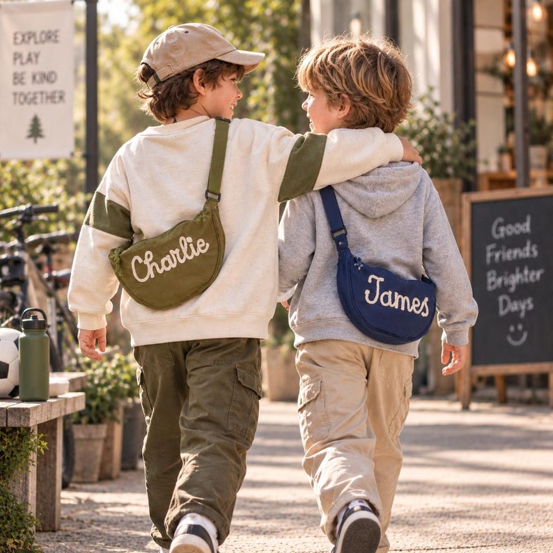 May include: Two crossbody bags made of canvas, one olive green with the name Charlie embroidered in white, and one navy blue with the name James embroidered in white. Both bags feature adjustable straps and are worn across the back.