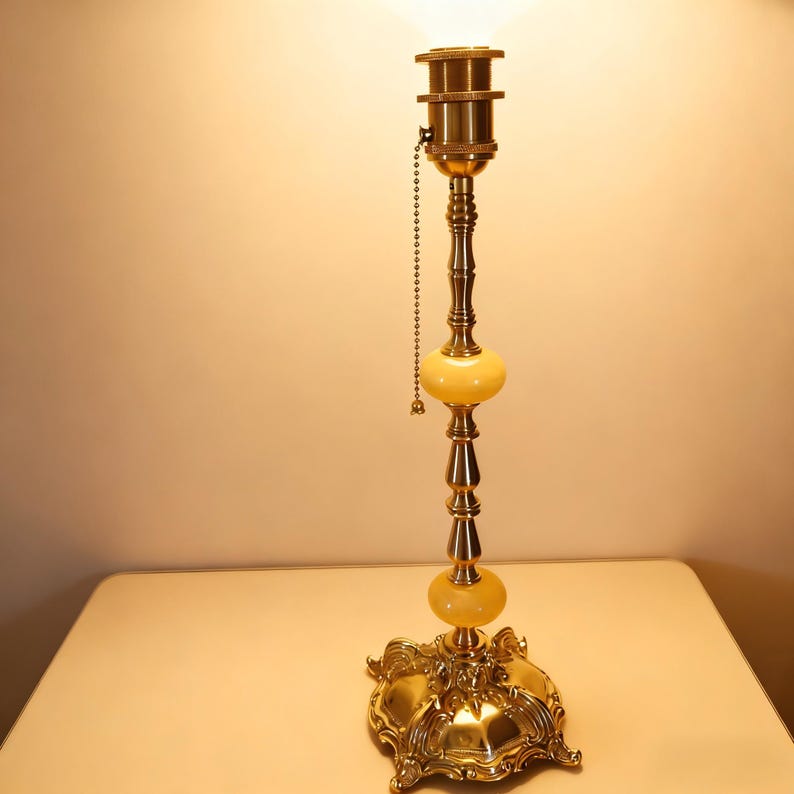 May include: A vintage brass table lamp with a decorative base and a chain pull. The lamp features two yellow-toned glass orbs and a detailed, ornate design. The lamp is on a light-colored surface.