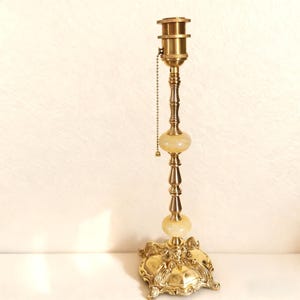 May include: A vintage brass lamp with a decorative base and two cream-colored orbs. The lamp has a pull chain and a detailed, ornate design. The lamp is a classic piece of home decor.